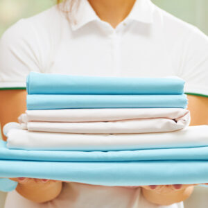 Closeup of woman's hand holding a stack of clean folded bed sheets of blue and white colors. Blurred background.